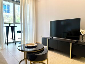 Relax in this stylish living room with a large flat-screen TV, round coffee table, and glass door leading to an outdoor area.
