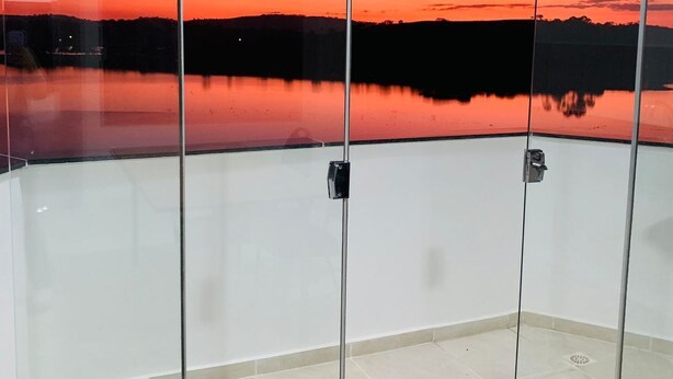 Een kamer met een glazen scheidingswand, uitzicht op een zonsondergang boven het water en een houten tafel.