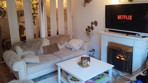 A cozy living room with a white sofa, a white coffee table, a fireplace, and a TV displaying 'NETFLIX'.