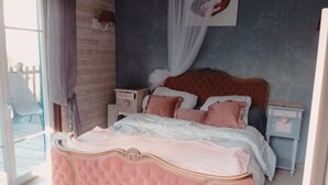 A bedroom with a large bed, a nightstand, a wall-mounted lamp, and a window with curtains.