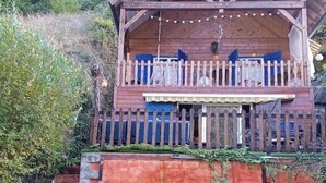 A wooden cabin with a balcony, a blue garage door, and a wooden fence.
