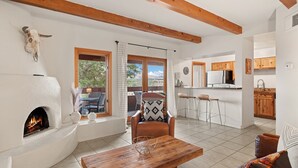 A spacious living area with a fireplace, a dining table, and a view of the outdoors. - Vista Serenity: Cozy Kiva, mountain views, 3 minutes from downtown (Santa Fe)