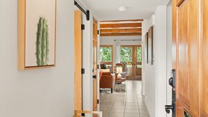 A hallway with wooden doors, a cactus artwork, a bench, and a view into a room with a chair and lamp. - Vista Serenity: Cozy Kiva, mountain views, 3 minutes from downtown (Santa Fe)