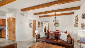A living room with a brown leather sofa, wooden coffee table, and a chandelier. - Vista Serenity: Cozy Kiva, mountain views, 3 minutes from downtown (Santa Fe)
