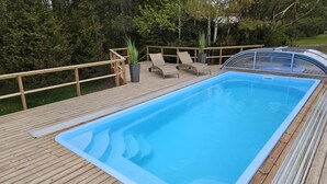 Een rechthoekig zwembad met een houten terras en ligbedden.