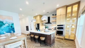 A modern kitchen with a central island, bar stools, wooden cabinets, and built-in appliances. - Brand New Luxury Beach House - Hot Tub (Galveston)