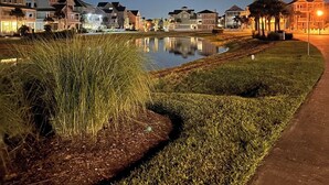A nighttime view of a residential area with houses, a pond, and a pathway. - Brand New Luxury Beach House - Hot Tub (Galveston)
