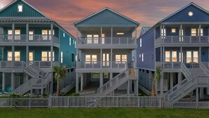 A row of three-story beachfront houses with balconies, a white picket fence, and a sunset sky. - Brand New Luxury Beach House - Hot Tub (Galveston)