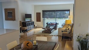 Ein modernes Wohnzimmer mit einem Holzespeisetisch, einem Fernseher und einem großen Fenster.