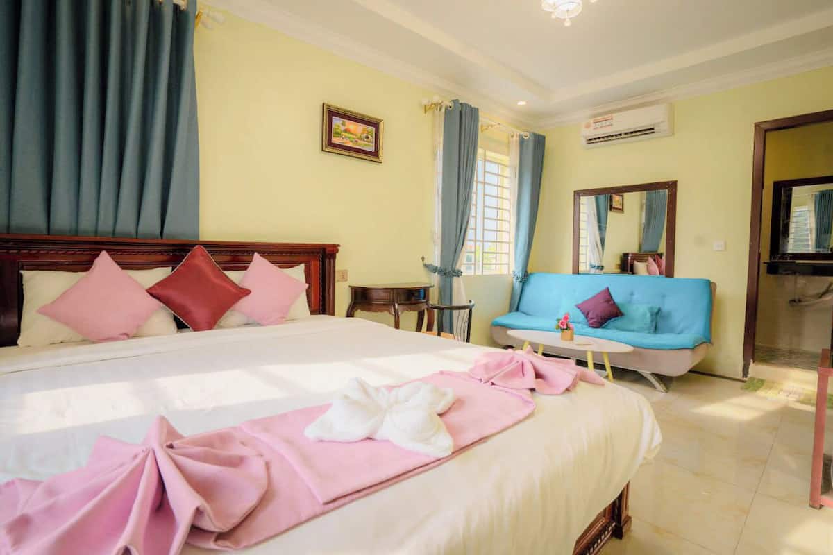 Una habitación de hotel con una cama grande, un sofá azul, una mesita y un espejo.