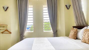 A hotel room with a large bed, two windows with curtains, a wooden headboard, and decorative wall sconces.
