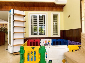 A room with a play area, a white shelf unit, and a window with blinds. - AHHA Boutique Kampot (Kampot)