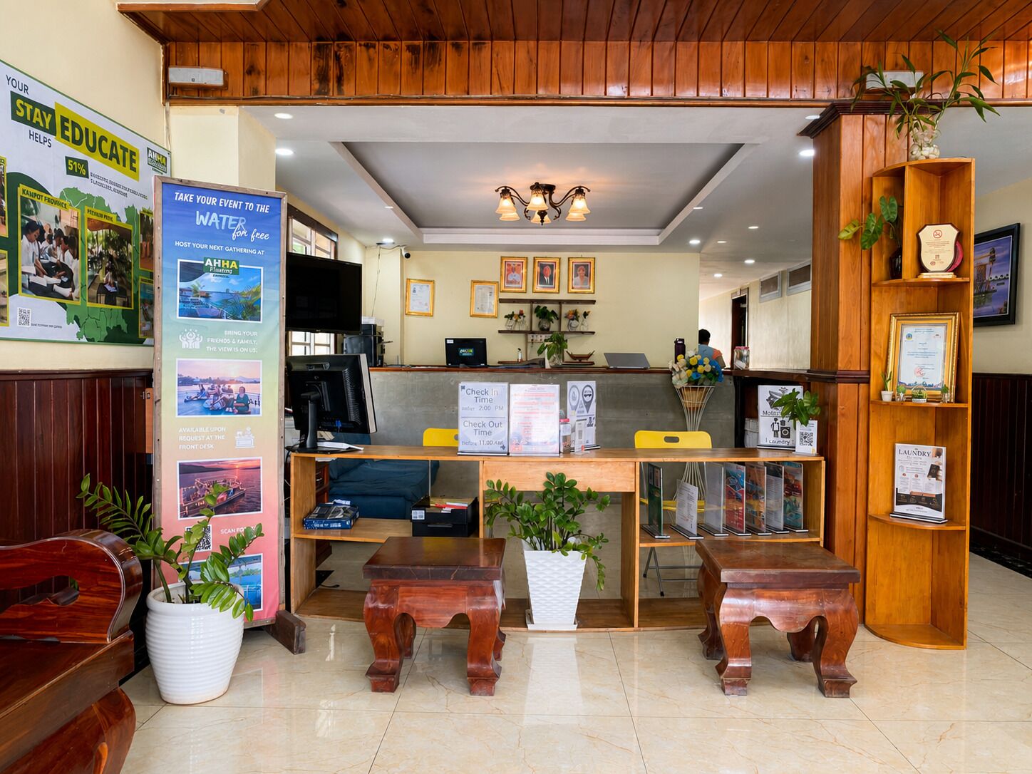 A reception area with a wooden desk, computer, and a check-in counter. There are potted plants and framed certificates on the walls.