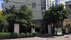 Un edificio de varios pisos con una llamativa franja vertical azul, una entrada protegida por una reja y un cartel que dice 'AHHA Boutique Kampot'.
