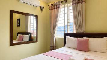 A hotel room with a bed, a large mirror, a window with curtains, and an air conditioning unit.
