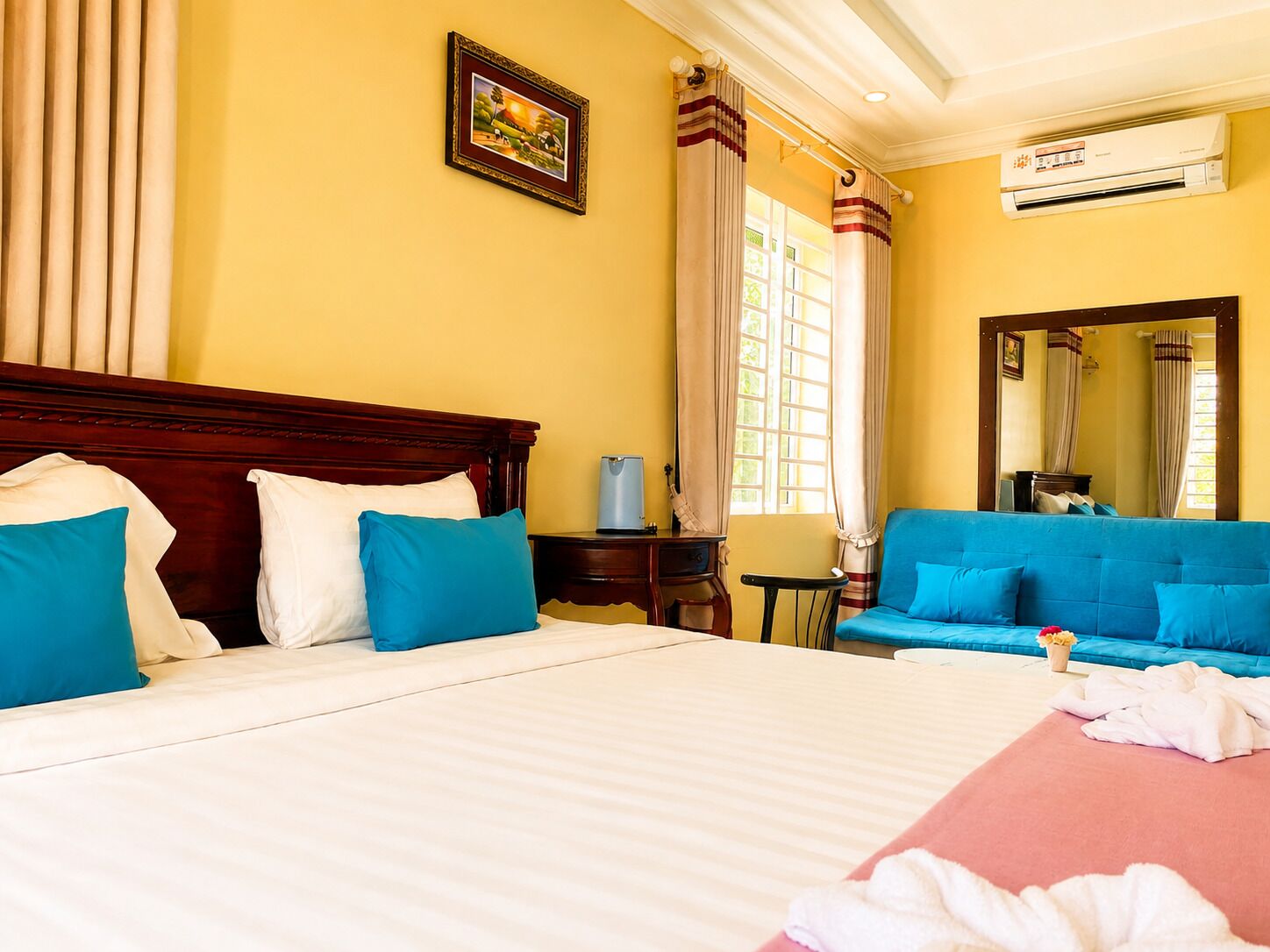 A hotel room with a large bed, a blue sofa, a small table, and a mirror.