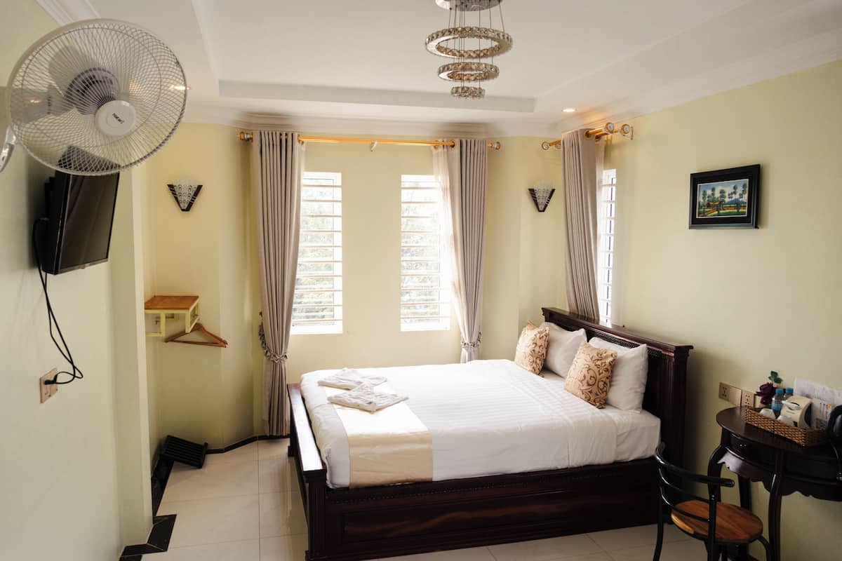Una habitación de hotel con una cama, un ventilador, un televisor, una mesita pequeña y una silla.