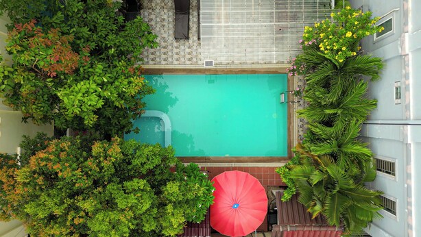 Vista aérea de una piscina rodeada de exuberante vegetación y un paraguas rojo.