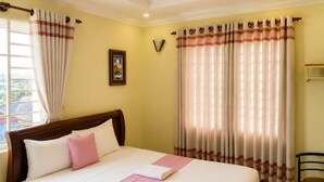 Quarto de hotel com cama, cortinas, um quadro na parede e luminária suspensa.
