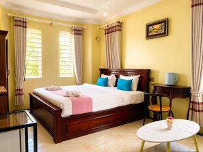 A hotel room with a large bed, bedside table, and a small round table with a vase. - AHHA Boutique Kampot (Kampot)
