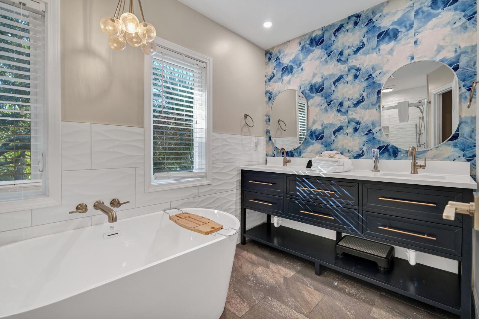 A modern bathroom with a freestanding bathtub, a vanity with a mirror, and a window with blinds.
