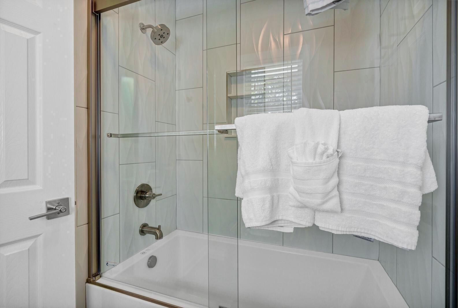 A modern bathroom with a glass-enclosed shower, a white bathtub, and a towel rack with two towels.