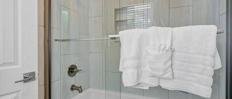 A modern bathroom with a glass-enclosed shower, a white bathtub, and a towel rack with two towels.
