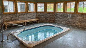 Ein Spa mit einem Whirlpool für 10 Personen, Steinwänden, Holzbalken und großen Fenstern.