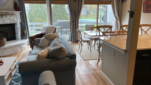 Ein Wohnzimmer mit Sofa, Kamin, Essbereich mit Tisch und Stühlen sowie Küchenzeile mit Arbeitsfläche und Schränken.