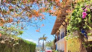 A narrow street with a car parked on the side, a building with a balcony, and a hedge on the left. - Vila do Pôr do Sol  (Aracati)