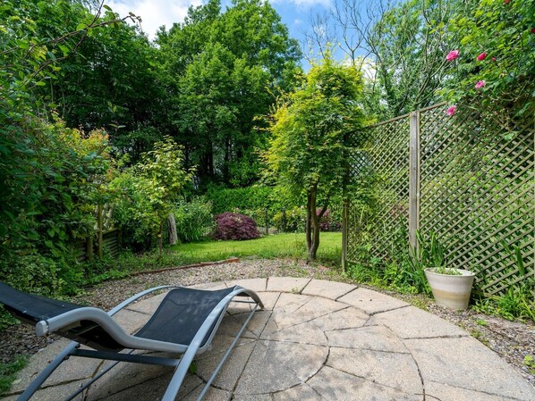 Een tuin met een stenen terras, een metalen stoel en een houten omheining.