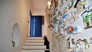 Een trap die leidt naar een kamer met een blauwe deur, een muur versierd met diverse kleine objecten en een stenen muur met een geschilderd tafereel.