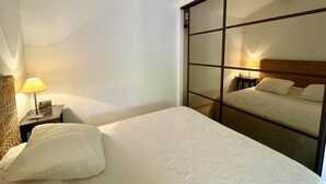 A hotel room with a bed, a nightstand, a lamp, and a large mirror reflecting the bed.