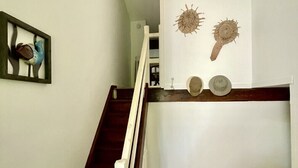 A staircase with a wooden handrail leading to a landing with a white wall. There are two decorative wall hangings and a framed picture on the wall.