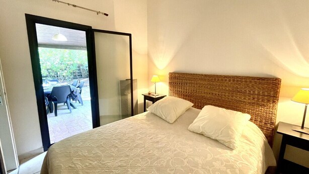 A hotel room with a large bed, a wicker headboard, two bedside lamps, and a sliding glass door leading to an outdoor seating area.