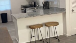 A modern kitchen with white cabinets, a granite countertop, and two wooden bar stools. - Metairie magic, 2 bedroom gem  (Metairie)