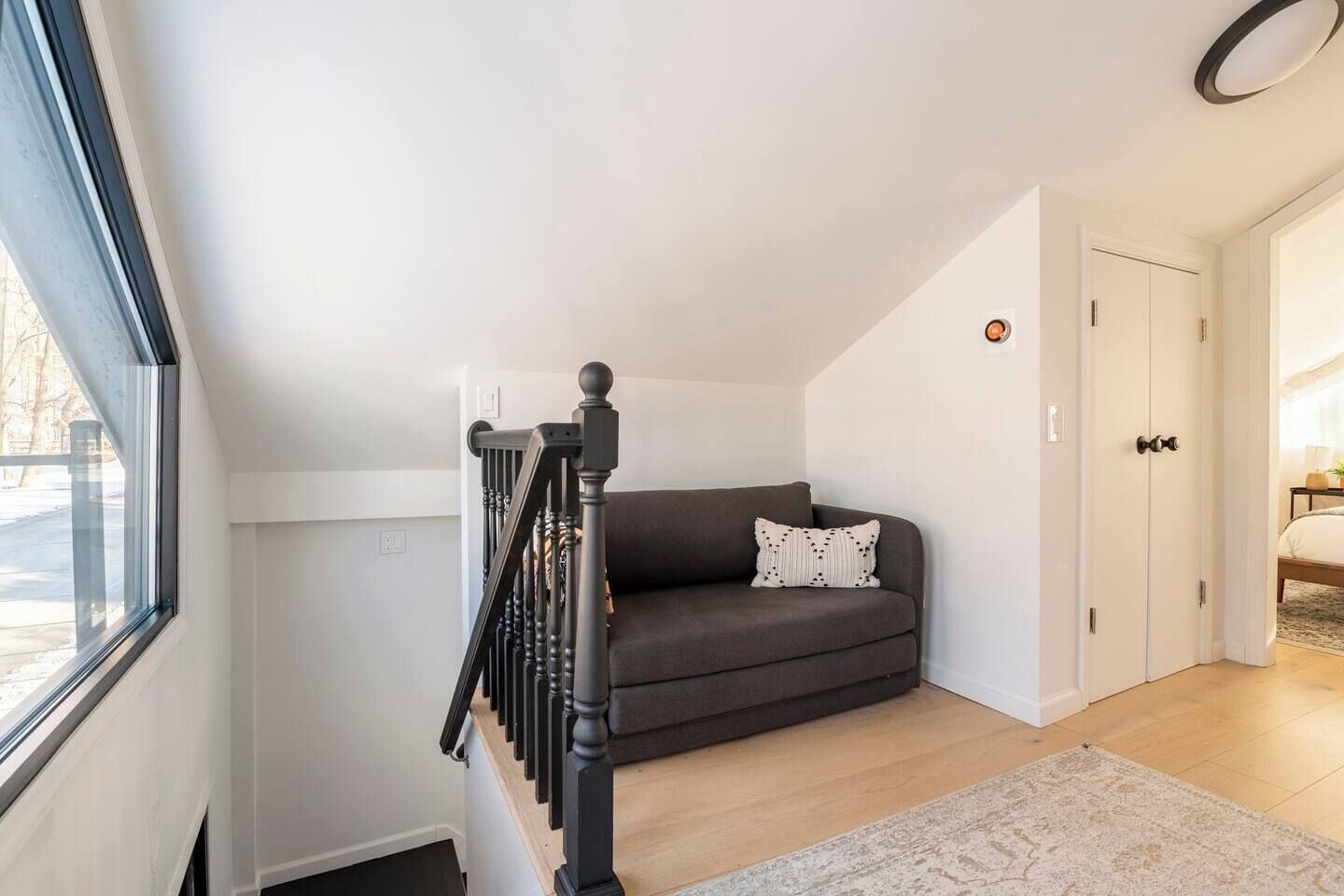 Een moderne woonkamer met een donkergrijze bank, een zwarte trap en een witte deur.