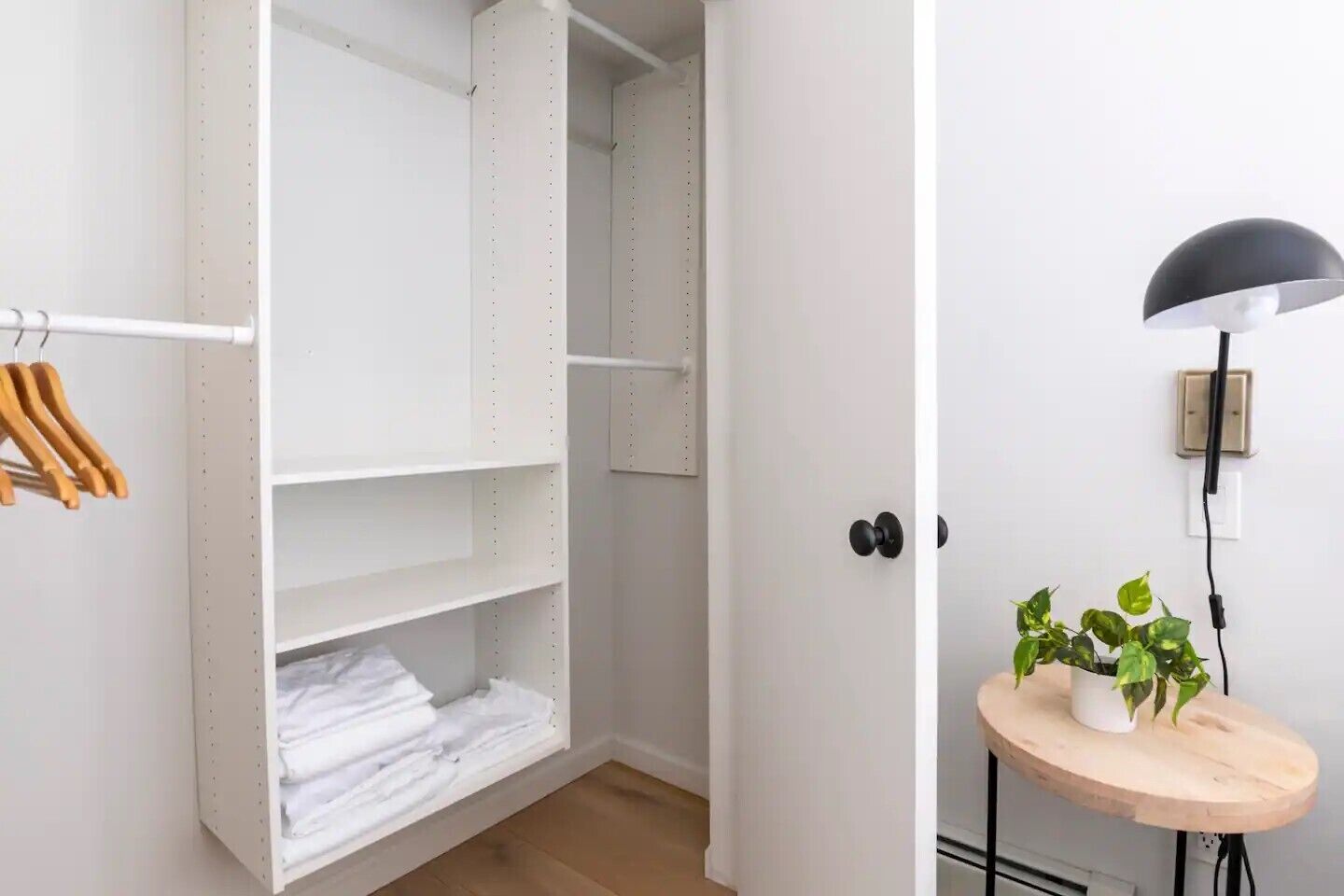 A walk-in closet with shelves and hanging space, a small round wooden table with a plant, and a black floor lamp.