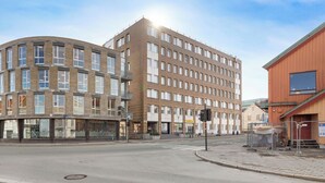 A multi-story building with a curved facade, a flat-roofed structure to the right, and a street intersection with a traffic light. - Heart of Trondheim (Trøndelag)