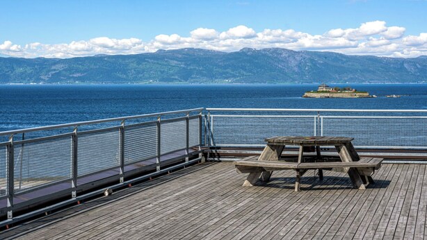 A wooden deck with a picnic table, overlooking a calm sea and distant mountains. - Heart of Trondheim (Trøndelag)