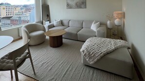 A modern living room with a sofa, a round coffee table, and a view of the city through large windows. - Heart of Trondheim (Trøndelag)