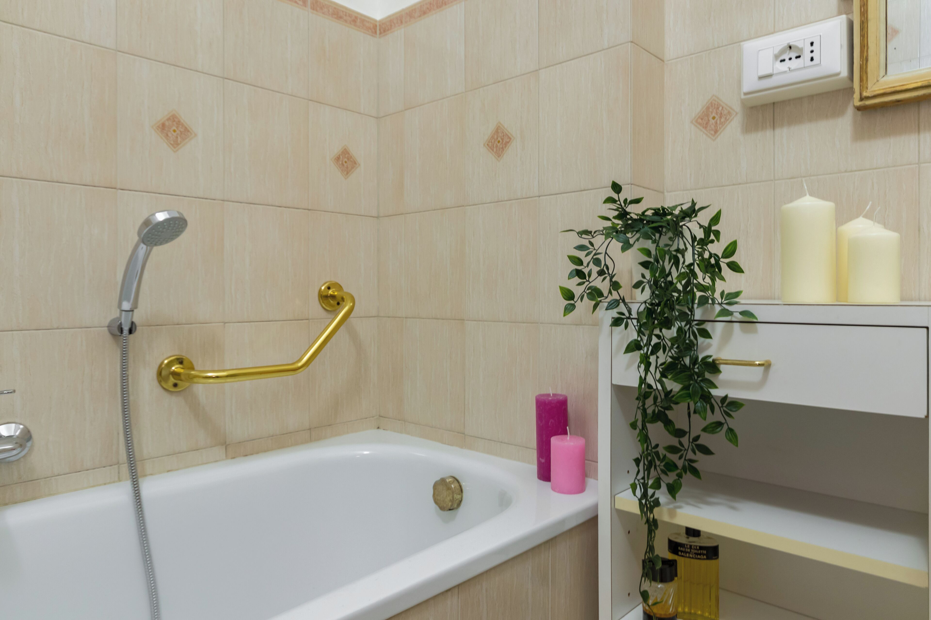 A bathroom with a bathtub, a shower, a gold grab bar, a pink candle, and a potted plant.