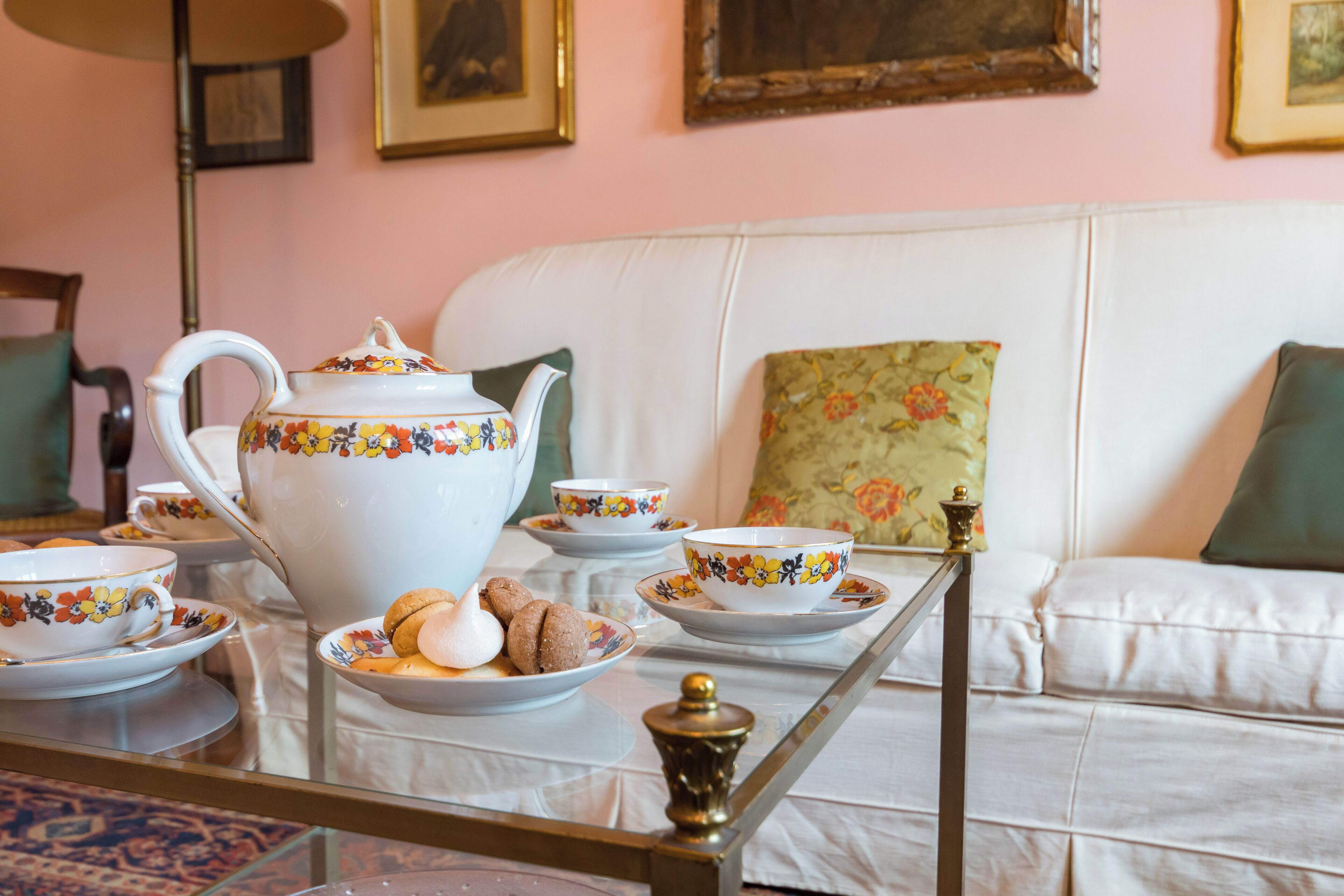 Un juego de té sobre una mesa de vidrio con un sofá blanco y cojines estampados en el fondo.