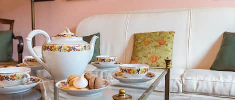 A tea set on a glass table with a white sofa and floral cushions in the background.