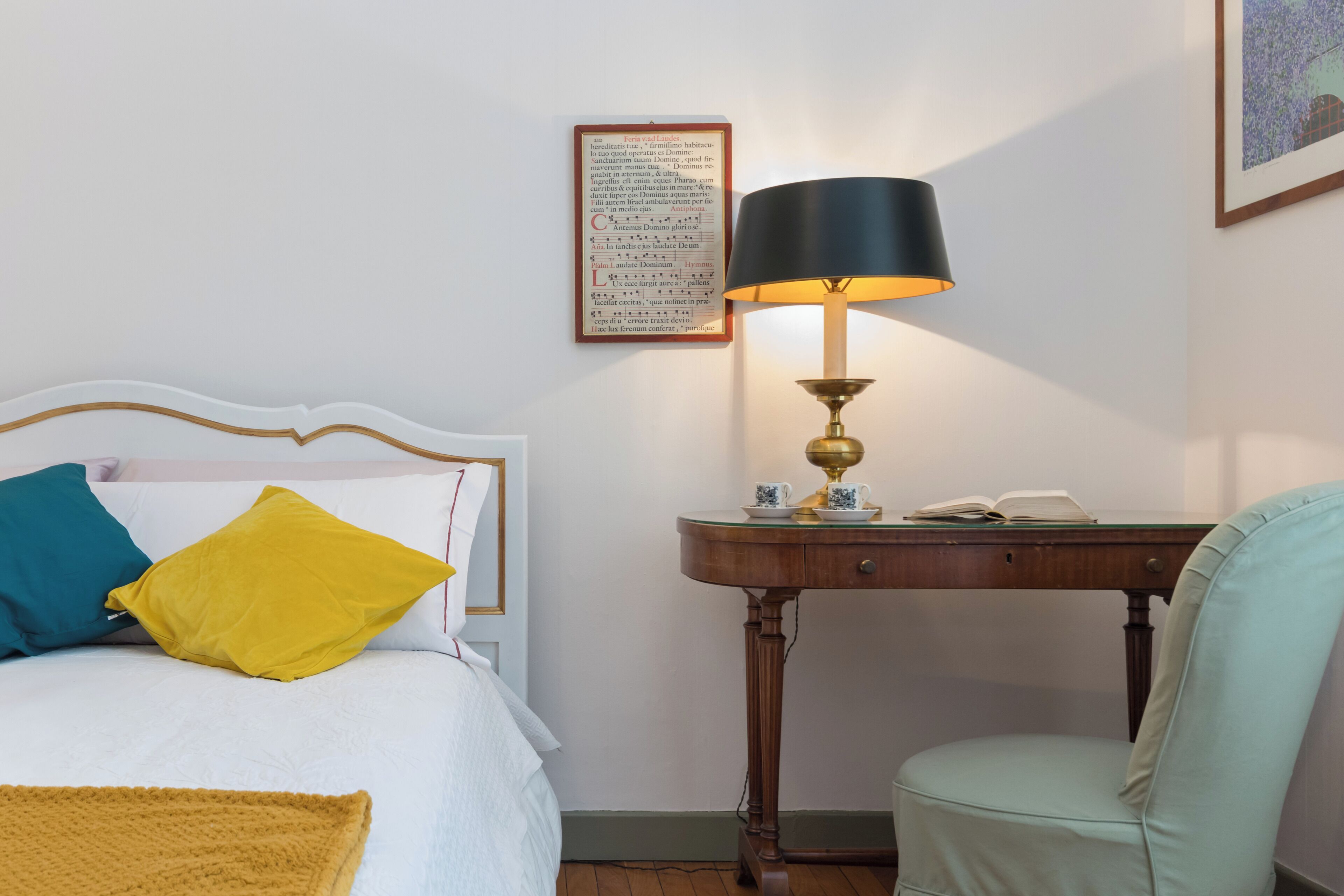 Et pænt opredt soveværelse med seng, sengebord med lampe, stol og et indrammet citat på væggen.