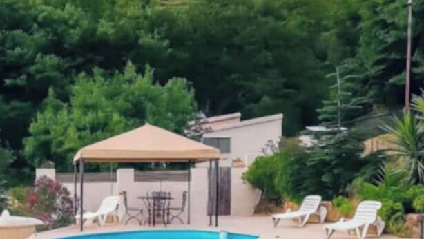 Zona de piscina con sillones de descanso y un pabellón, rodeada de follaje y una montaña al fondo.