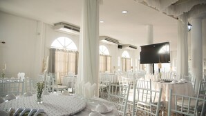 A banquet hall with round tables, white chairs, and a large screen. - Bananaleaf Wedding Cafe & Resort (Nakhon Chai Si)