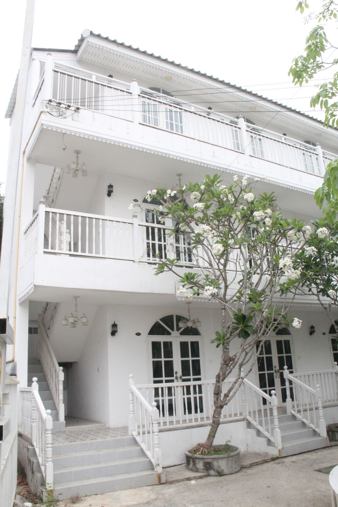 A two-story building with white exterior walls, a balcony on the upper floor, and a staircase leading to the entrance.
