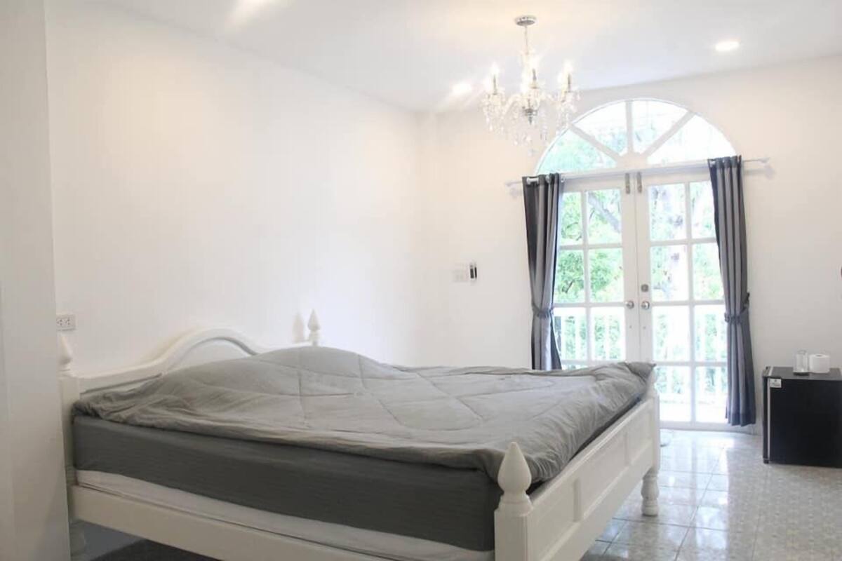 Une chambre à coucher avec un lit, un lustre, une fenêtre avec des rideaux et une porte donnant sur l’extérieur.