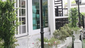 A white building with a balcony, outdoor seating, and decorative street lamps. - Bananaleaf Wedding Cafe & Resort (Nakhon Chai Si)